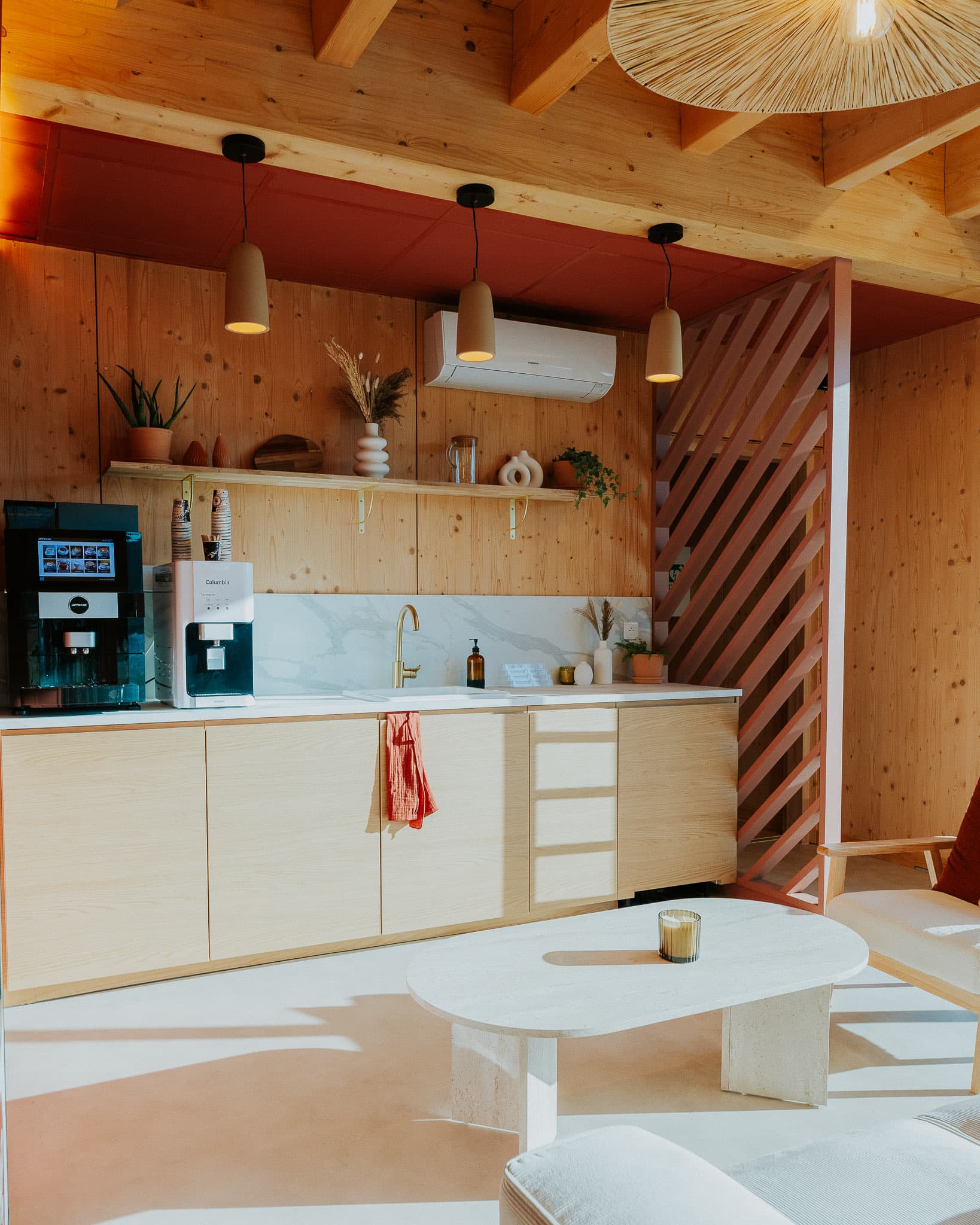Espace café : cuisine en bois clair, bandeau terracotta et table basse en pierre